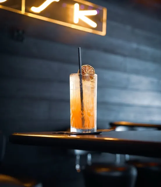 A long orange cocktail on a dark bar under the DUSK sign