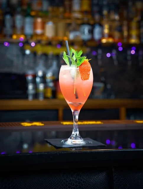 A strawberry and mint spritz in front of a lit back bar