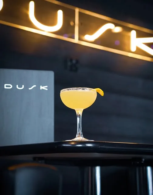A yellow cocktail on the bar beneath the DUSK neon sign