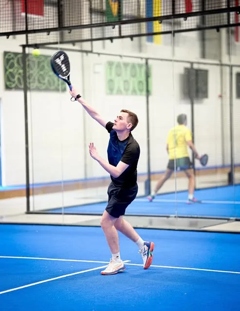 A padel player reaching for a smash on a blue court